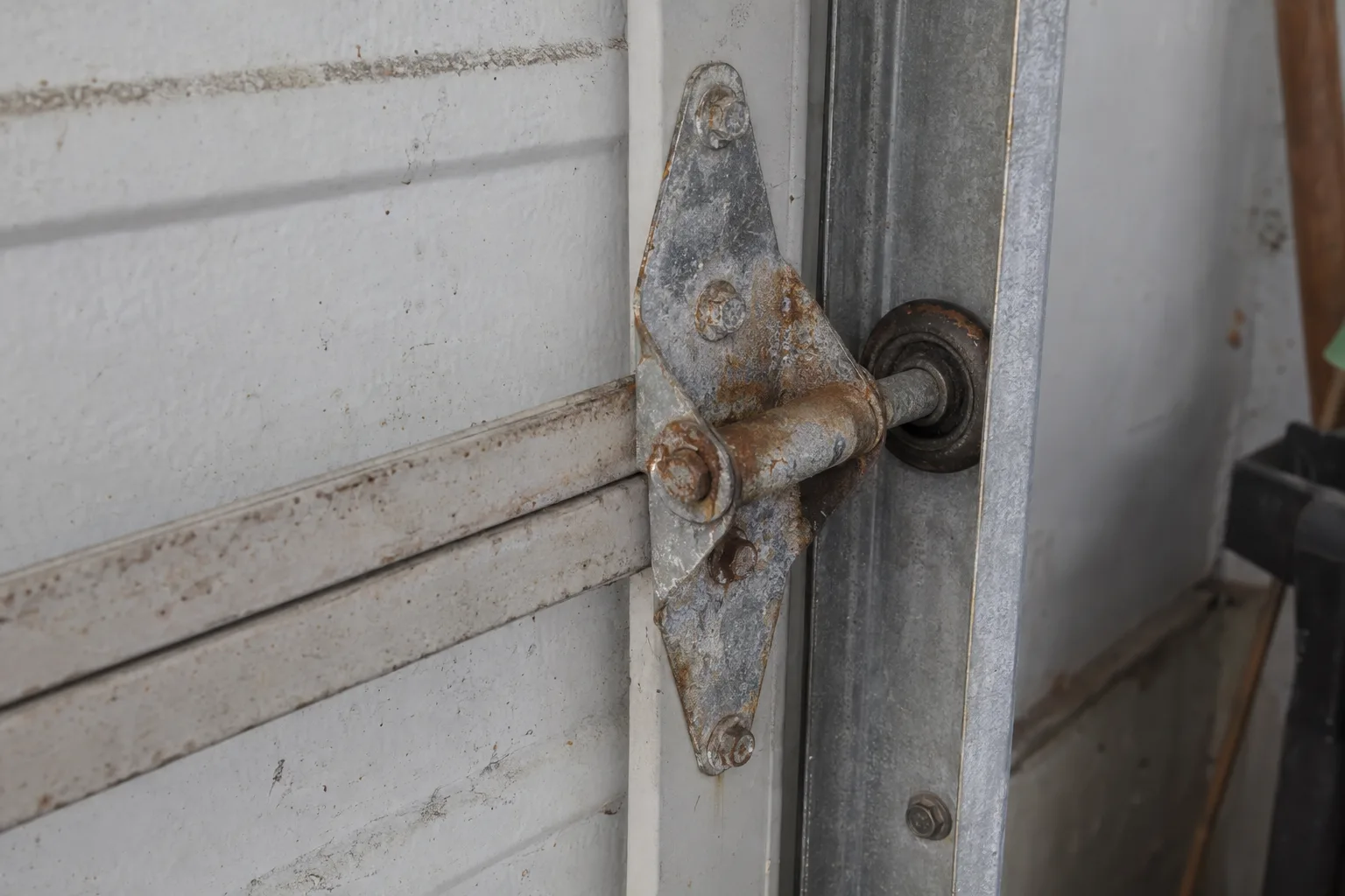 Corroded steel hinges and rusted bolt heads on an older garage door, showing orange surface rust and white salt oxidation on the metal hardware in close detail