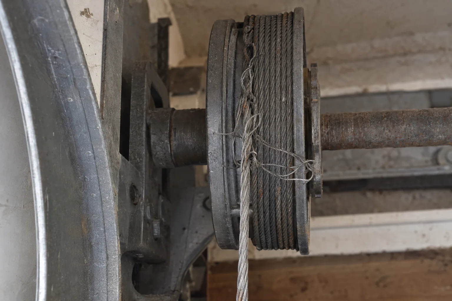 Frayed and corroded galvanized steel cable strands close to a garage door drum, showing surface rust and unraveling wire filaments