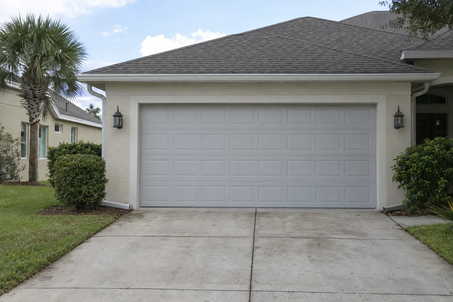 New insulated double-car garage door on a pale stucco two-car garage in a sunny Florida suburban neighborhood, with a manicured lawn and palm tree visible