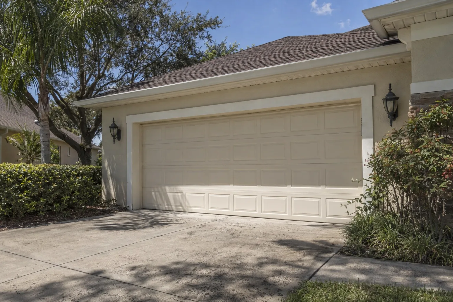 West-facing attached two-car garage on a Florida suburban home bathed in intense afternoon sunlight, with palm trees and live oak visible in the foreground under a bright blue sky