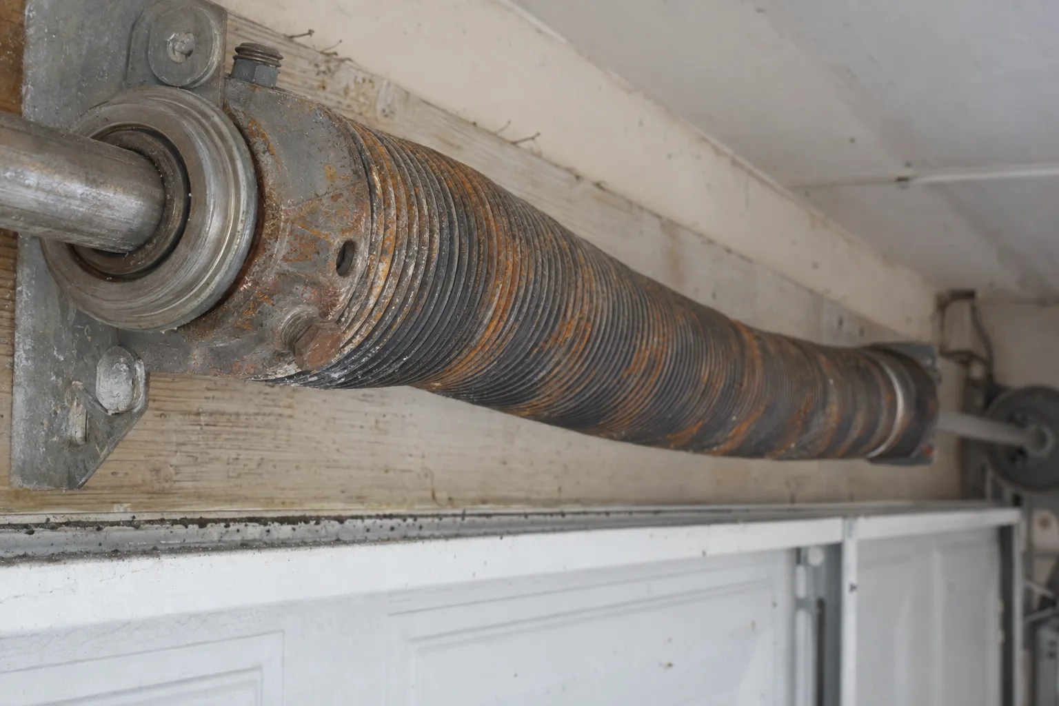 Close-up of a corroded orange torsion spring coil mounted above a residential garage door, showing rust and surface deterioration