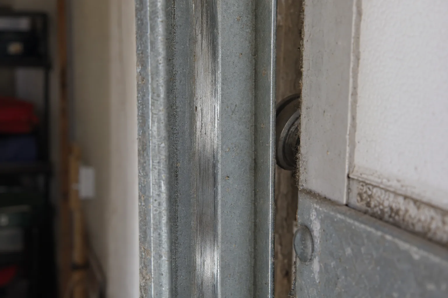Close-up view of the inner wall of a steel garage door track showing a polished groove worn into the painted metal surface where rollers have repeatedly made contact and caused friction damage.