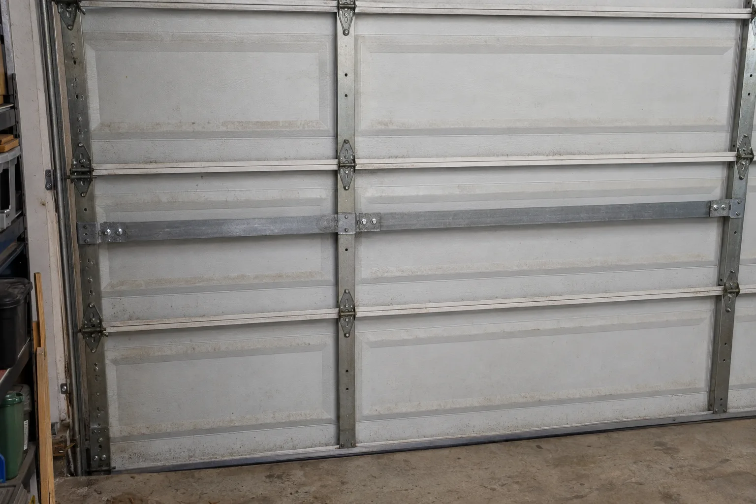 Galvanised steel horizontal bracing strut bolted across the inside of a sectional garage door panel, viewed from inside the garage